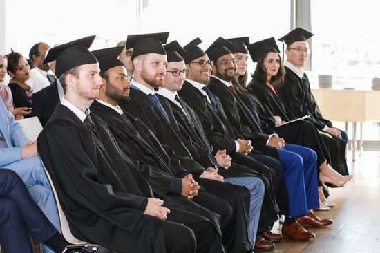 Gruppe Studierende sitzend in schwarzen Talaren mit schwarzer viereckiger Kappe
