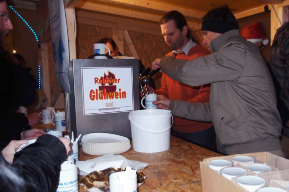 TUW-Kollegen beim Ausschenken im Punschstand. Winterlich gekleidet; Häferl im Vordergrund.
