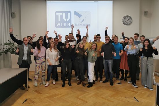 Gruppe Mentor_innen stehend in Raum vor Leinwand mit TU Logo