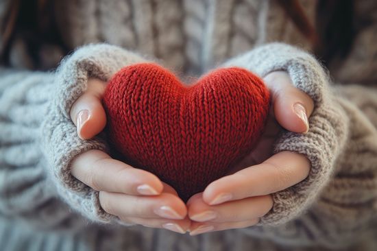 A photo of two hands holding a knitted heart
