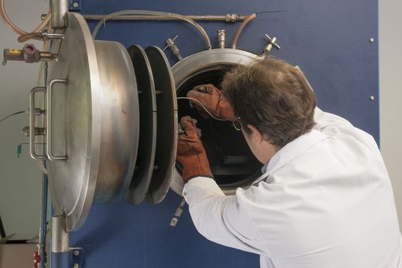 Ein Mitarbeiter holt Teile bei geöffnter Ofentüre mit einer Zange aus dem Rohofen.