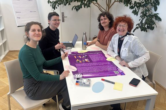 Vier Personen sitzen rund um einen Tisch und blicken freundlich in die Kamera.