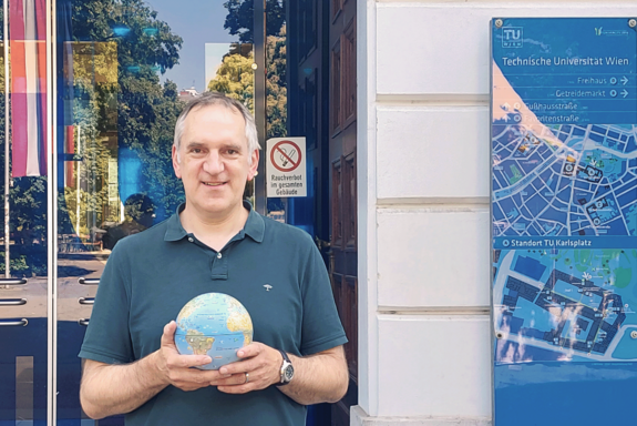 Martin Berens vor dem Haupteingang der TU Wien. Er hält einen kleinen Globus in der Hand. 