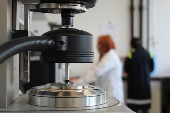 Gerät zur Untersuchung von Bitumen, im Hintergrund zwei Menschen