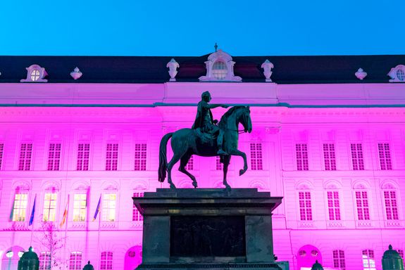 Gebäude lila beleuchtet, Reiterstatue im Vordergrund