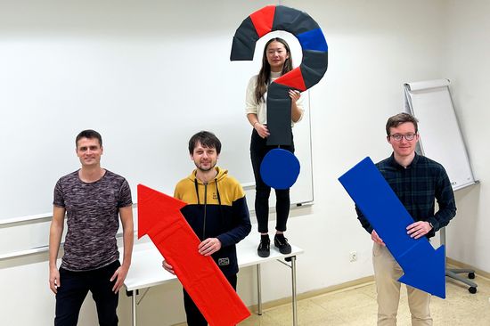 Four people, three of whom are standing in a triangle. Two are holding an arrow, one is holding a question mark.