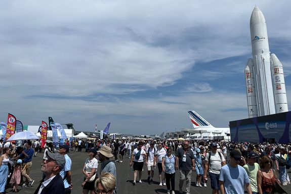 Platz voller Menschen, Flugzeuge und eine Rakete. Bewölkter Himmel.