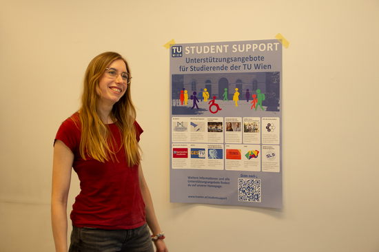 Lisa Vrablitz lächelnd mit rotem T-Shirt und Brille, daneben ein buntes Plakat