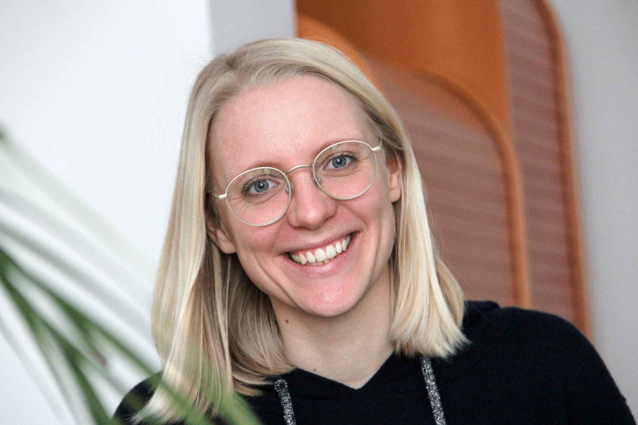 Dinah Gaffal, lächelnd, mit schwarzem Pullover, links im Vordergrund der verschwommene Zweig einer Palme.