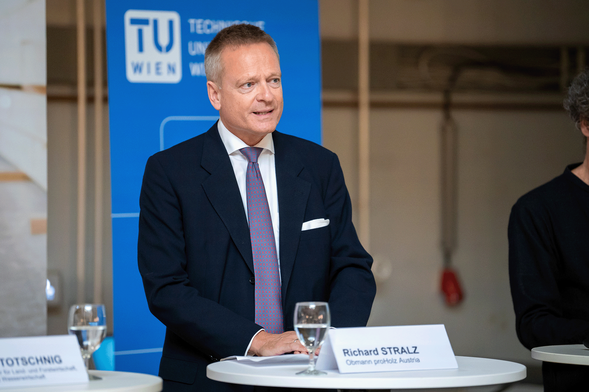 Richard Stralz mit dunkelblauem Jackett, weißem Hemd und Krawatte am Rednerpult.