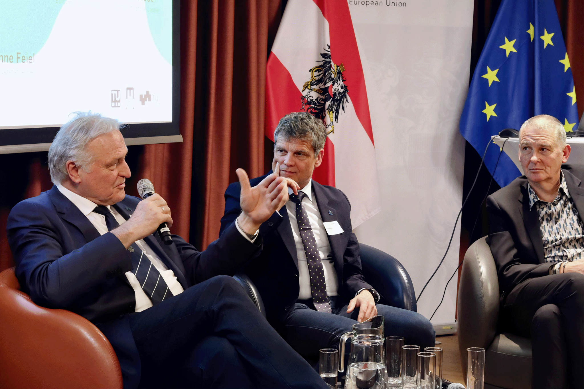 Podiumsdiskussion. Ein Mann spricht mit Mikro, zwei hören zu