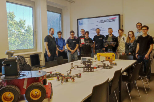 Students holding two racing cars, standing behind a table with several robots