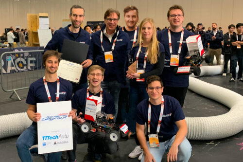 Group picture of the team with cars and trophy