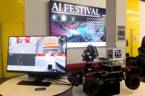 Screen, racing car and sign of AI festival in the background.