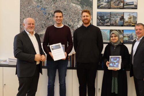 Gruppe vor Stadtplan und Baustellenbildern v.l.n.r.: Josef Eberhardsteiner (Vizerektor für Digitalisierung und Infrastruktur), Markus Pietschmann, Clemens Rauber (Ansprechperson für Studierendenthemen im .digital office), Aslihan Sasmaz und Bernd Logar (Leiter des .digital office) bei der Preisübergabe