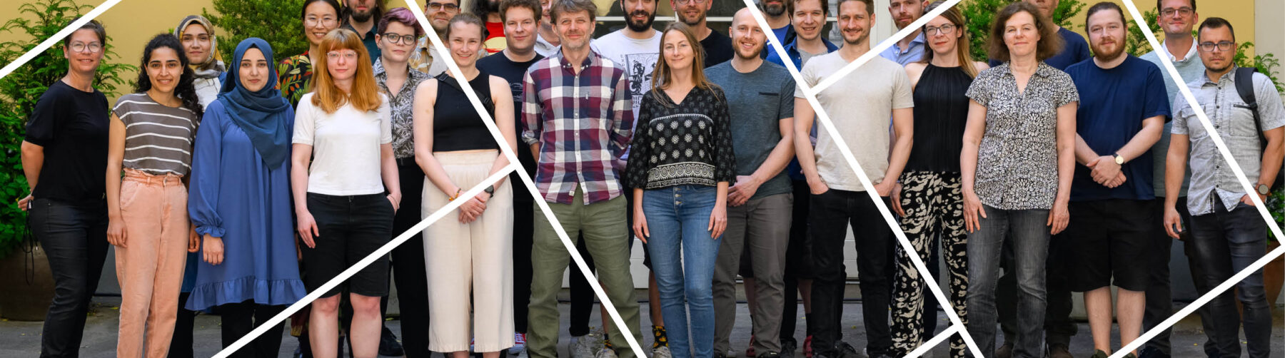 Headerbild mit Gitternetzlinien Gruppenfoto Personen stehend vor gelben Haus, großes Fenster in der Mitte, Sträucher im Hinetrgrund sichtbar