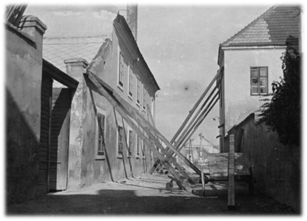 Schwarz-weiß Bild von Häusern nach einem Erdbeben, die von Holzbalken gestützt werden